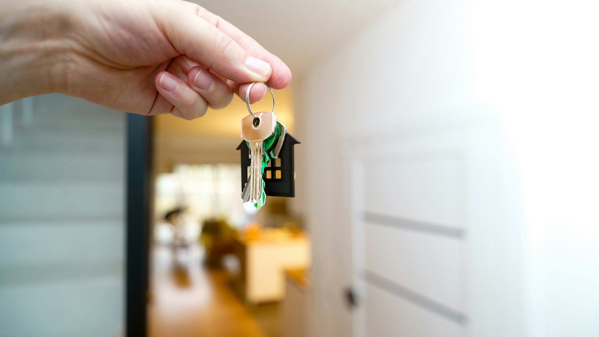 A hand holding a set of house keys in a bright hallway