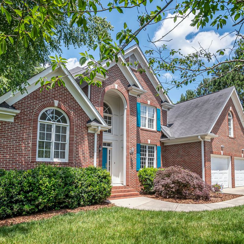 A red brick two-story house with blue shutters and a green lawn